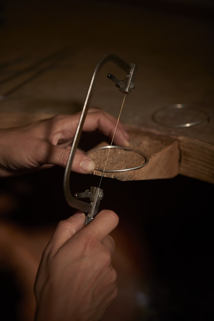 On voit les mains de la créatrice de bijoux Louise Vurpas en train de couper un bracelet sur un bracelet au-dessus de son établi. Bijouterie-joaillerie sur-mesure